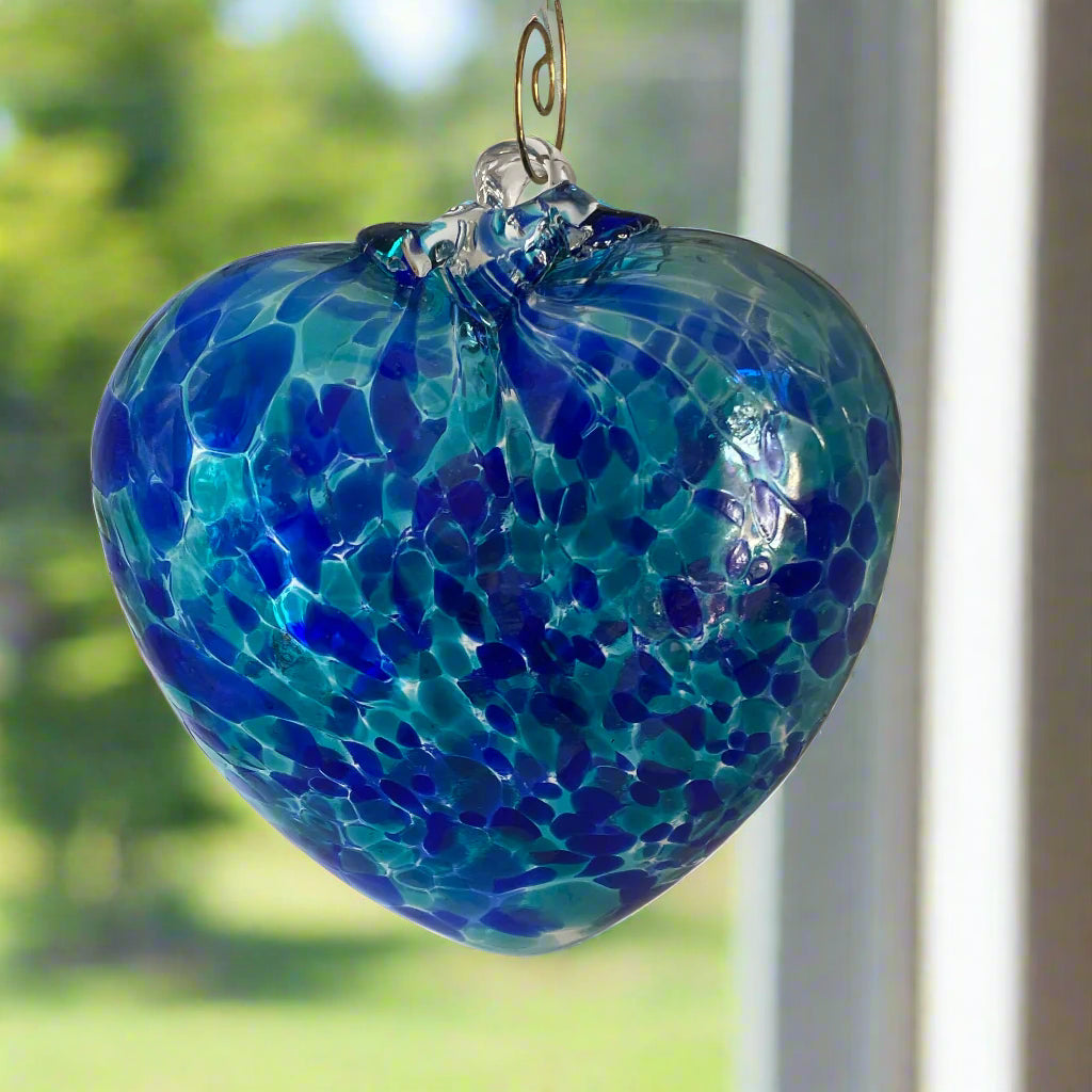 2 Sisters Artisan Glass 4 inch Blown glass heart ornament with aqua blue and cobalt speckles. Blown glass suncatcher hanging in a window.